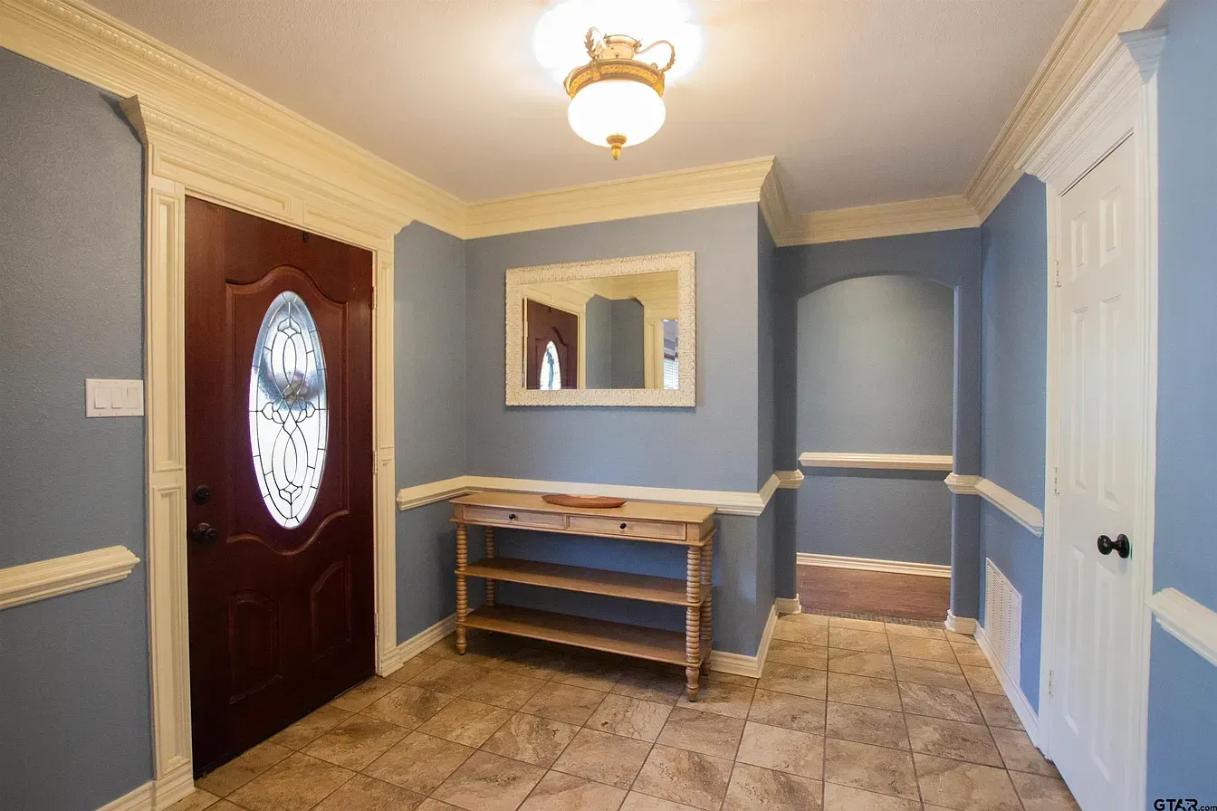 Blue entryway with tiled floor, white trim, oval glass front door, and wooden bench under a wall mirror