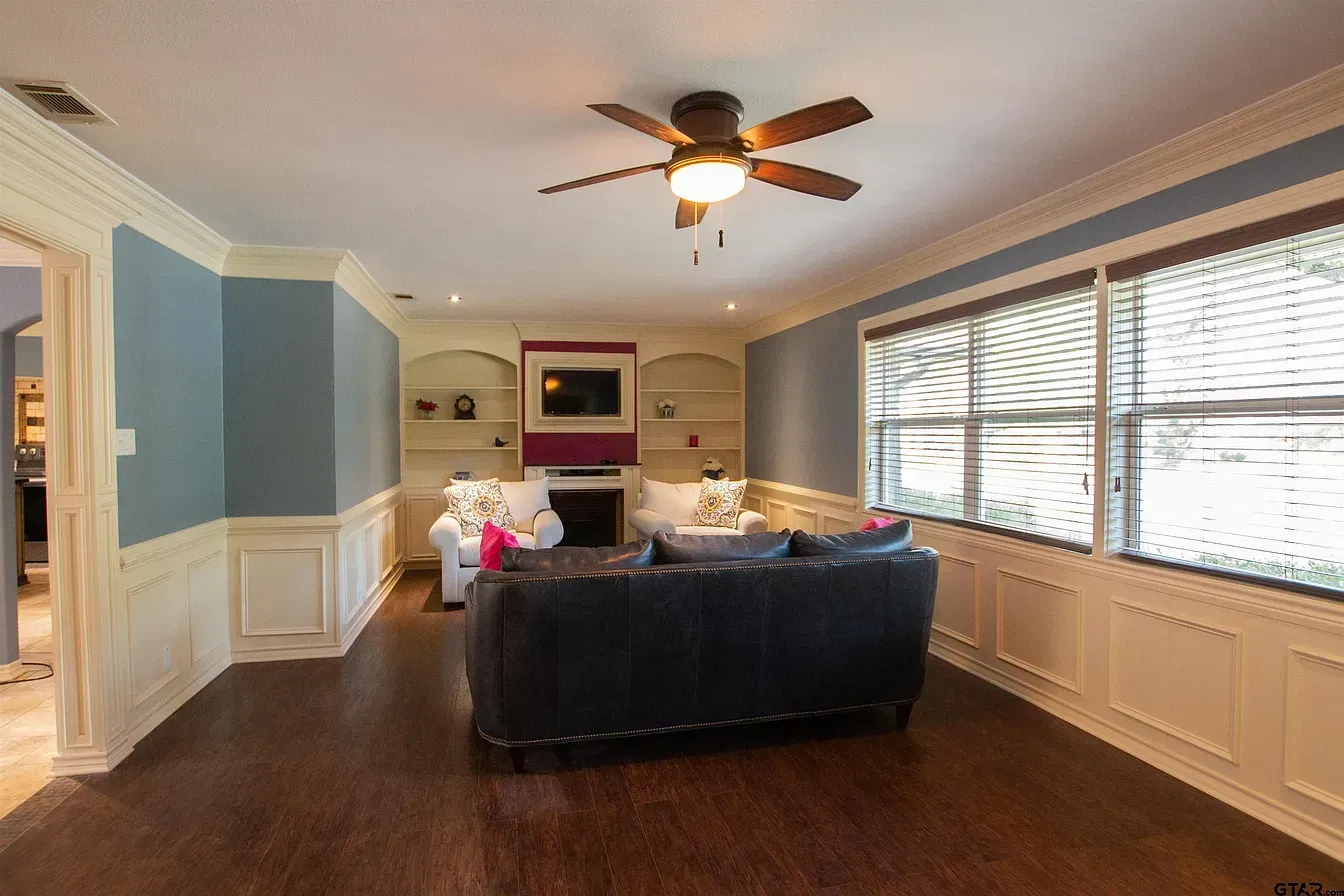 Bright living room with blue walls, leather sofa, fireplace, large windows, and ceiling fan