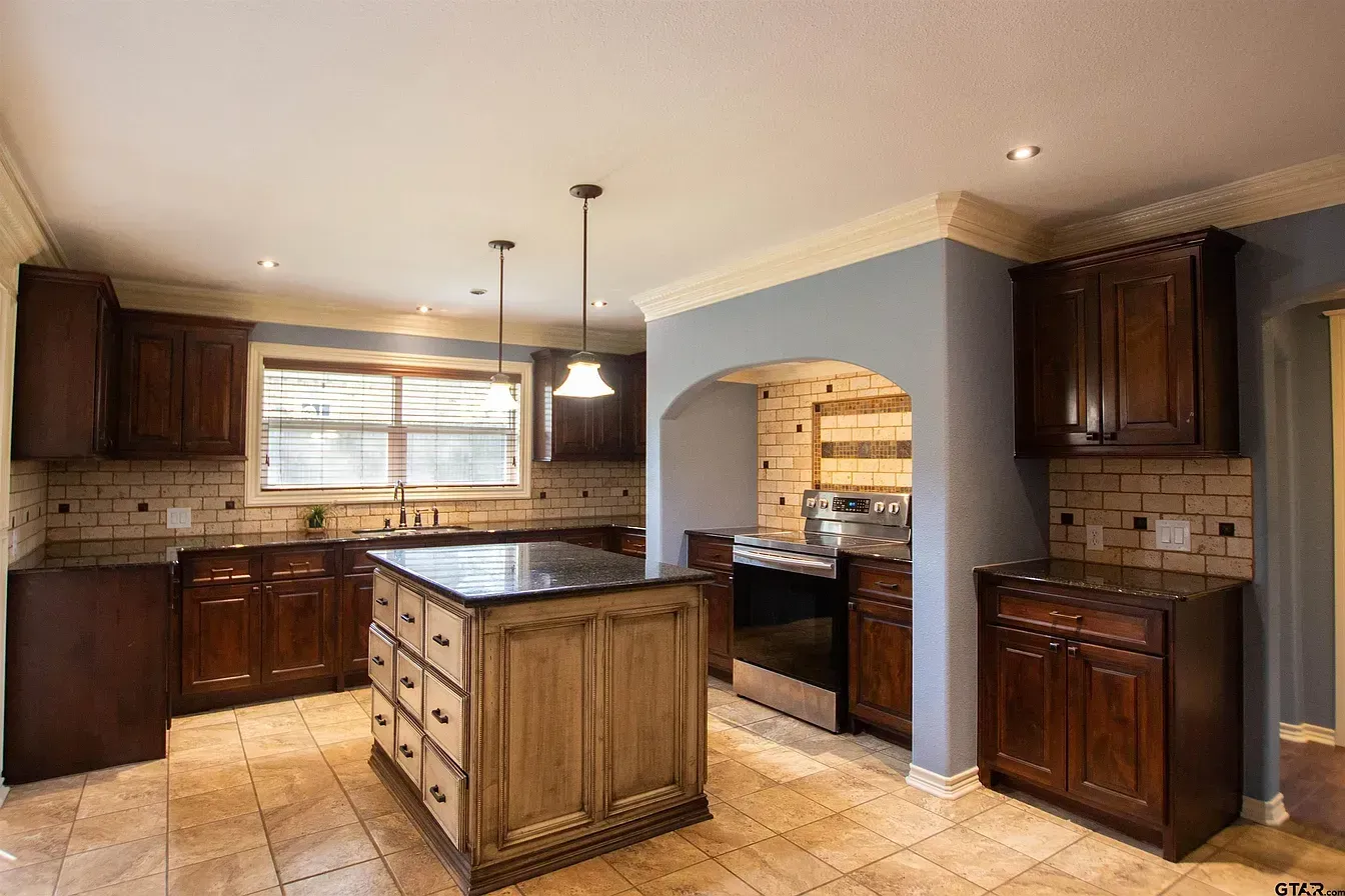 Spacious kitchen with dark wood cabinets, central island, tiled floors, and arched pass-through opening
