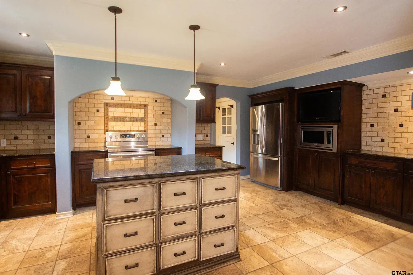 Modern kitchen with wooden cabinets, granite island, stainless steel refrigerator, and brick backsplash