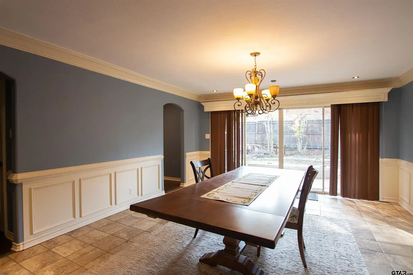 Elegant dining room with a long wooden table, chandelier, large window, and tiled floor