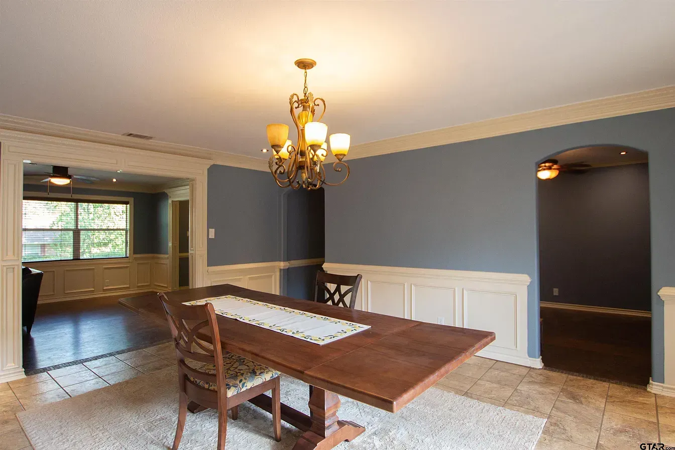 Dining room with wooden table, chairs, chandelier, and adjacent living area with blue walls.