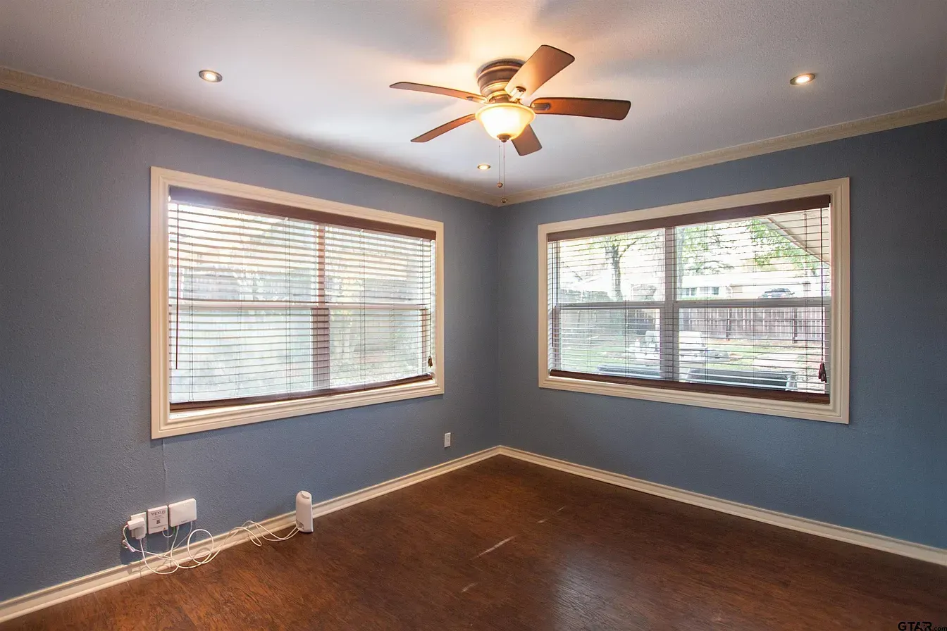 Empty blue bedroom with two windows, ceiling fan, and dark wood floor
