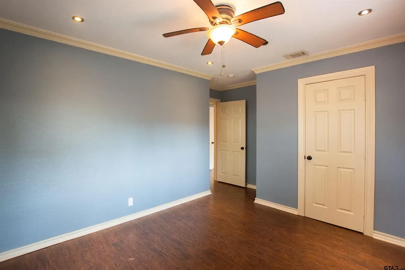 Empty blue bedroom with ceiling fan, hardwood floors, and white doors
