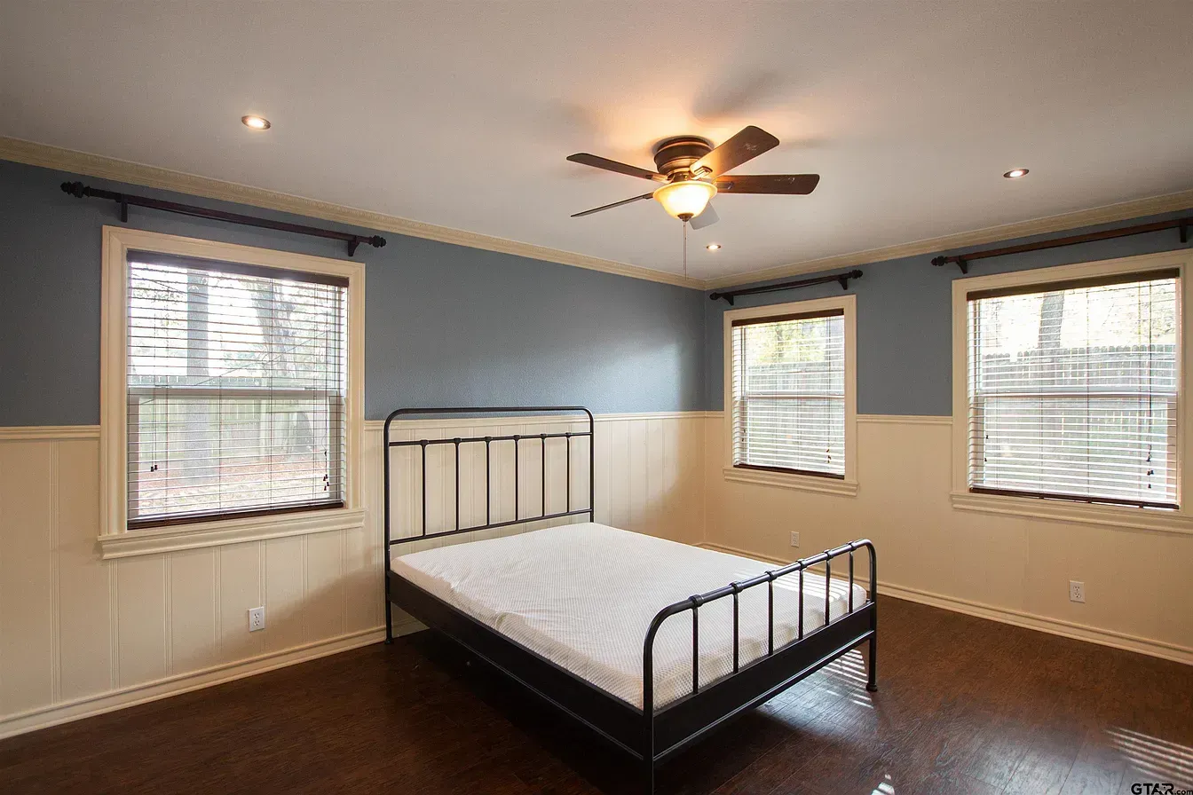 Empty bedroom with metal bed frame, blue walls, brown carpet, and three windows with blinds.