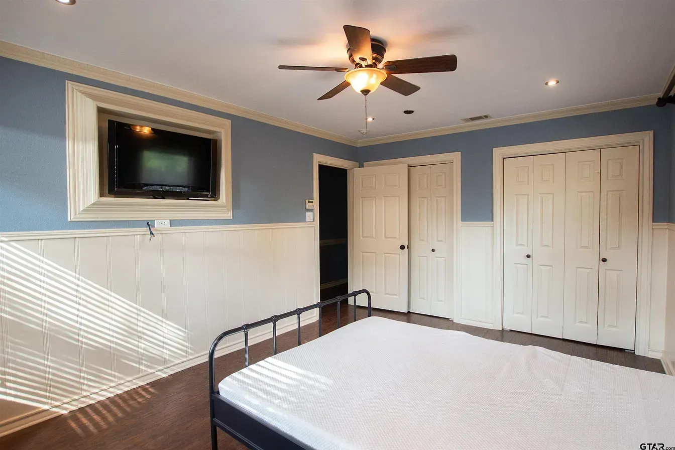 Bedroom with blue walls, ceiling fan, wall-mounted TV, and a metal-framed bed with a white comforter