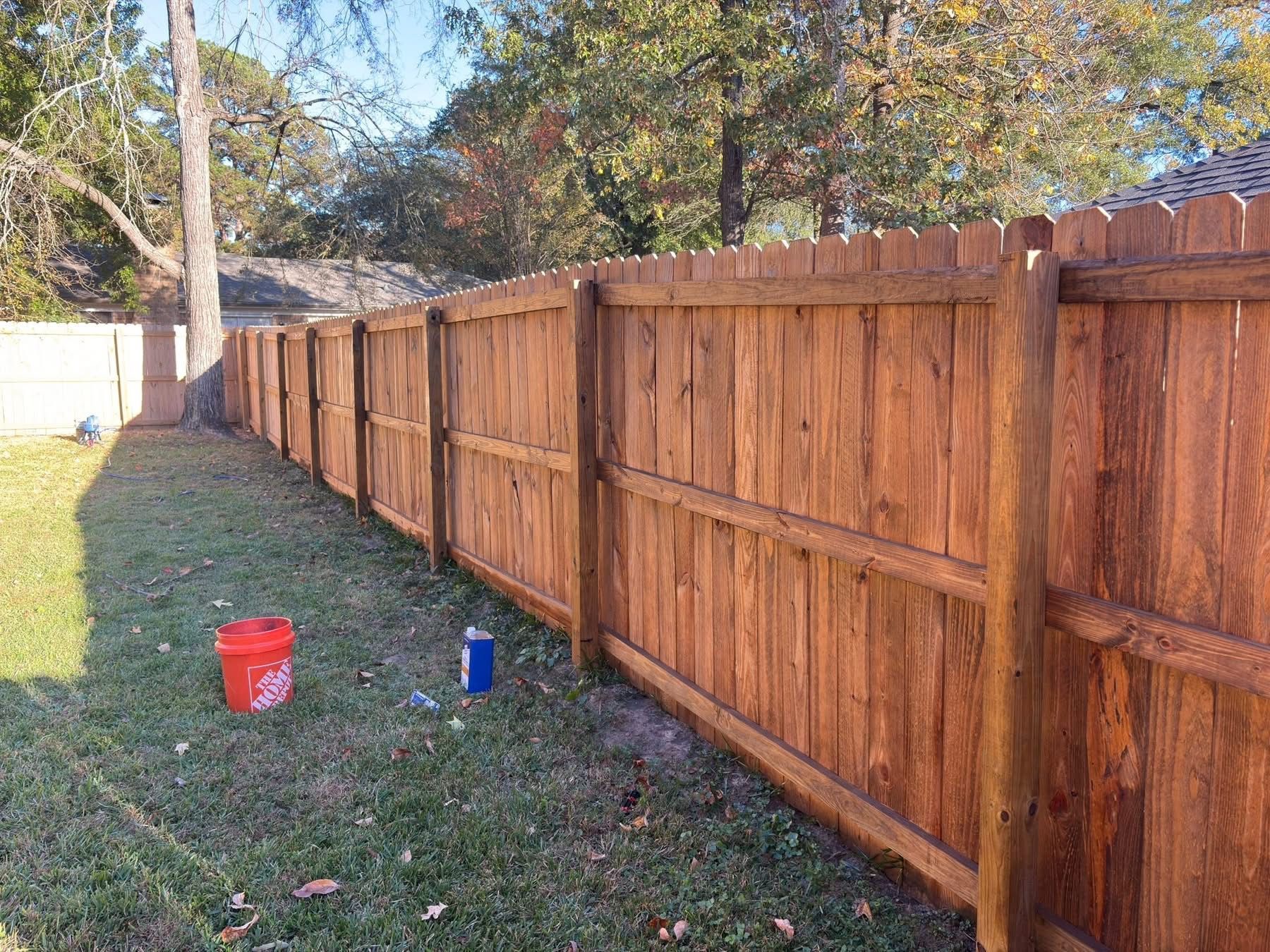 Wooden privacy fence along a grassy yard with a red bucket and blue cup near the fence