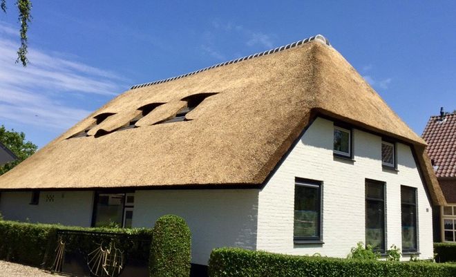 Een wit huis met een rieten dak en dakramen.