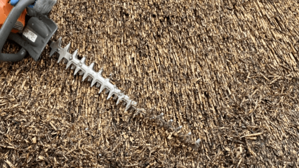 Een heggenschaar knipt een hoop bruin gras.