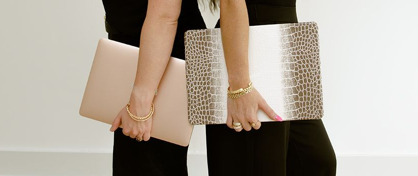 Two people hold beige and light pink laptops against a white wall.