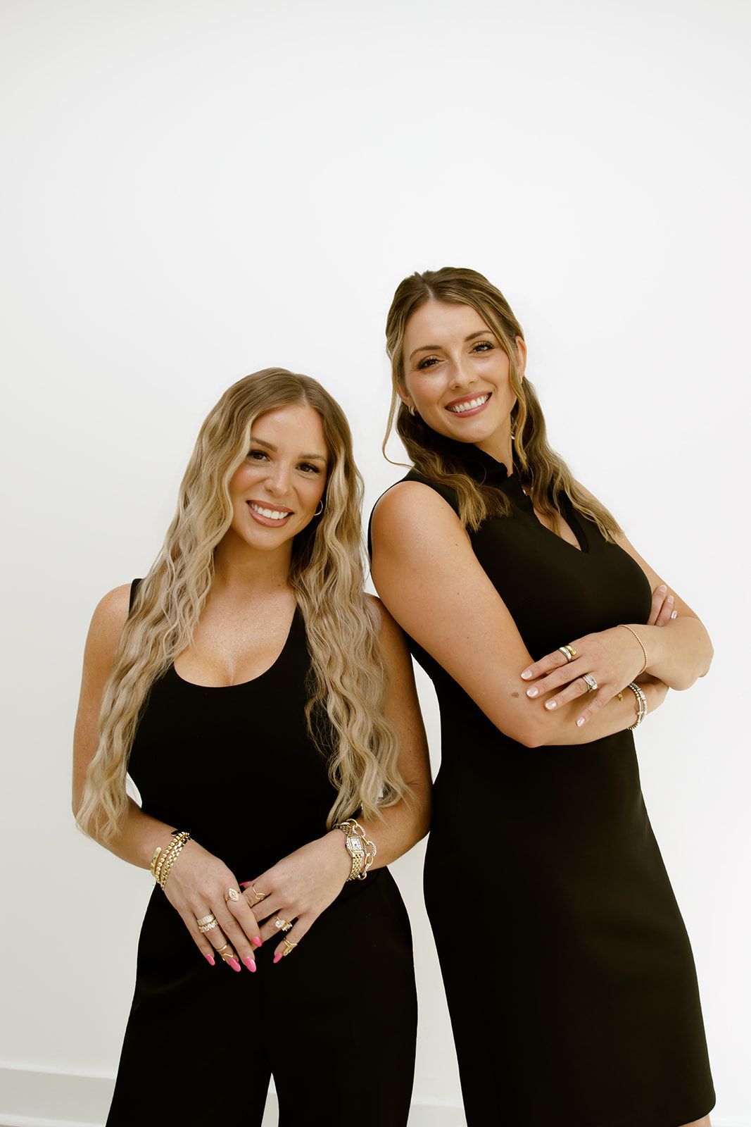 Two women in black dresses posing and smiling against a white studio background
