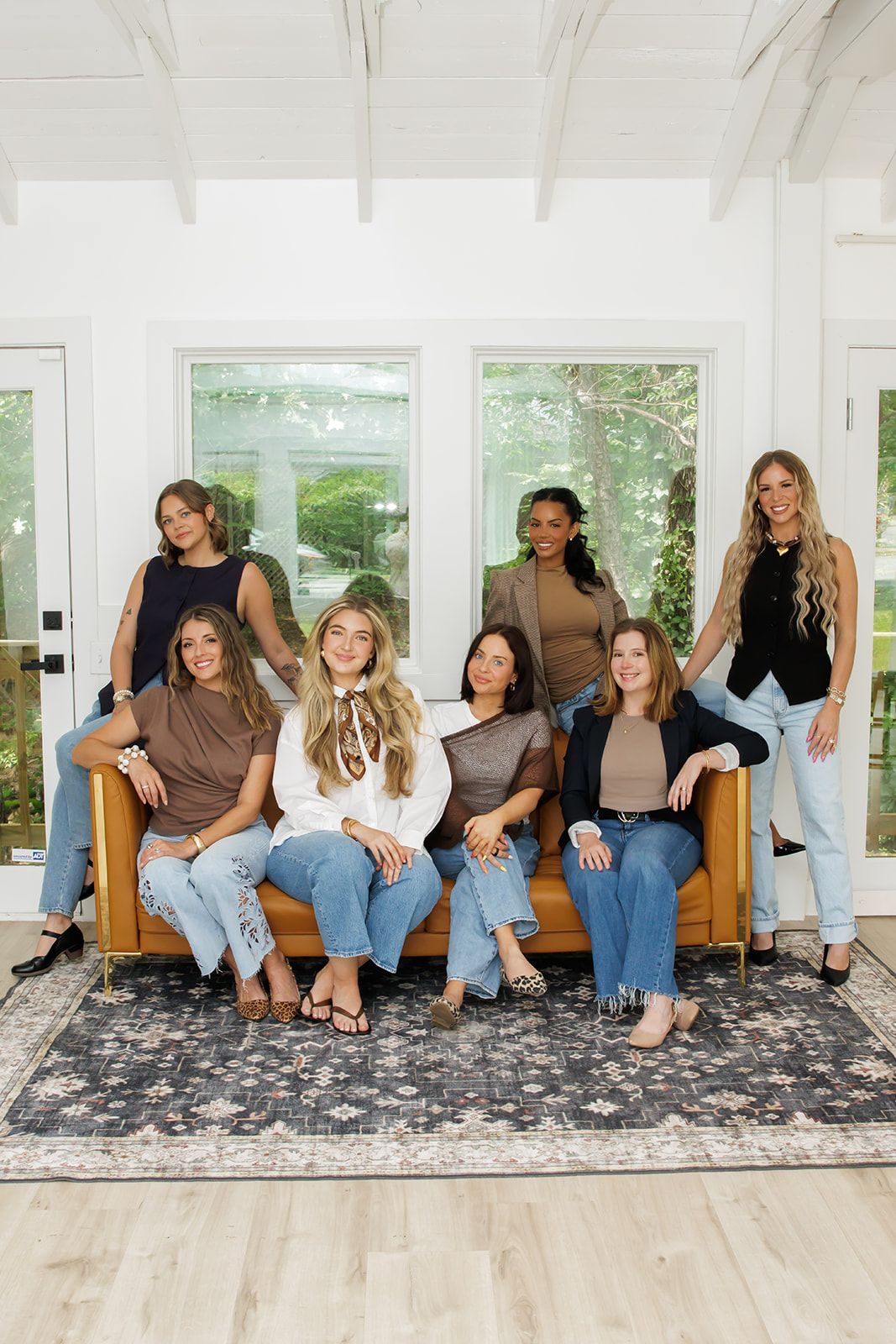 Seven people pose in a bright living room with a blue couch, white walls, and a large patterned rug.