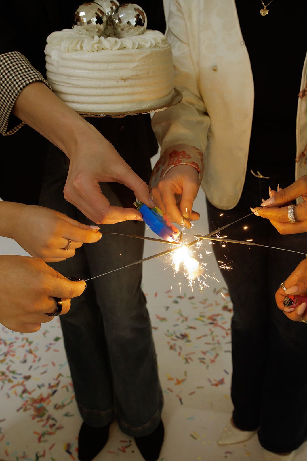 People cutting a white frosted cake with sparklers at a celebration.