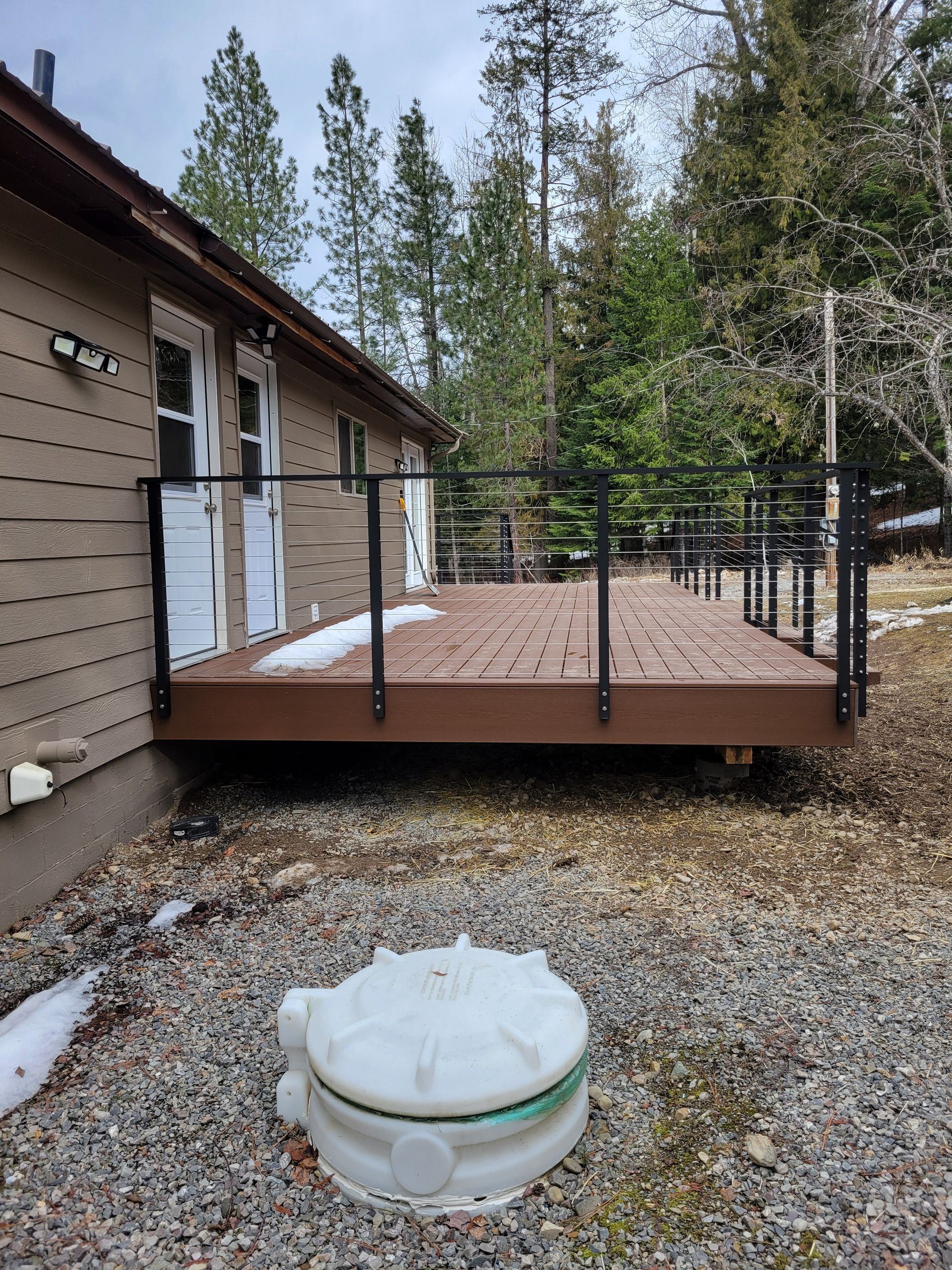 Brown deck with black railing outside a beige house; a white septic tank is in front.