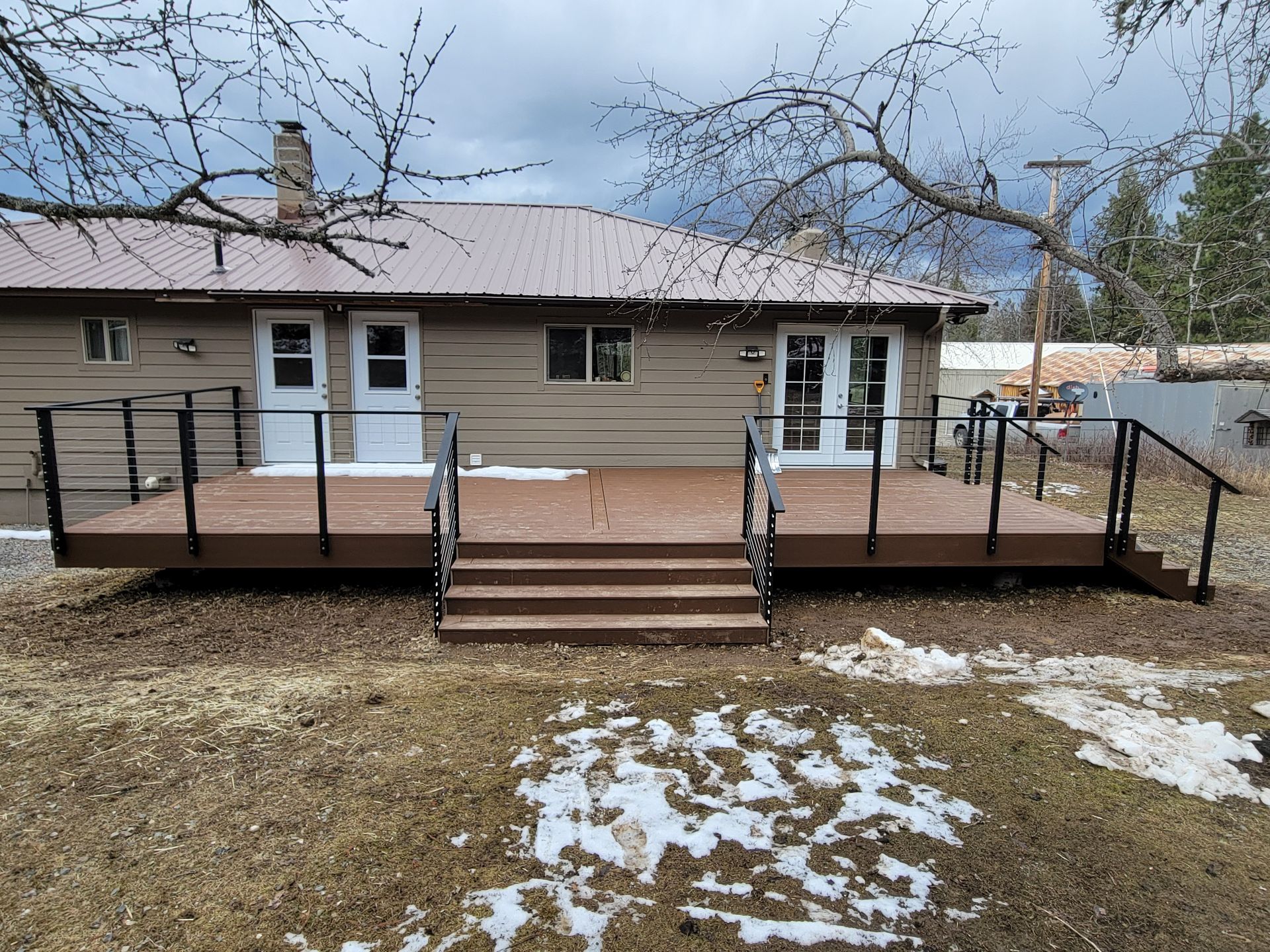 Backyard deck with brown composite boards, black railing, and steps leading to yard.