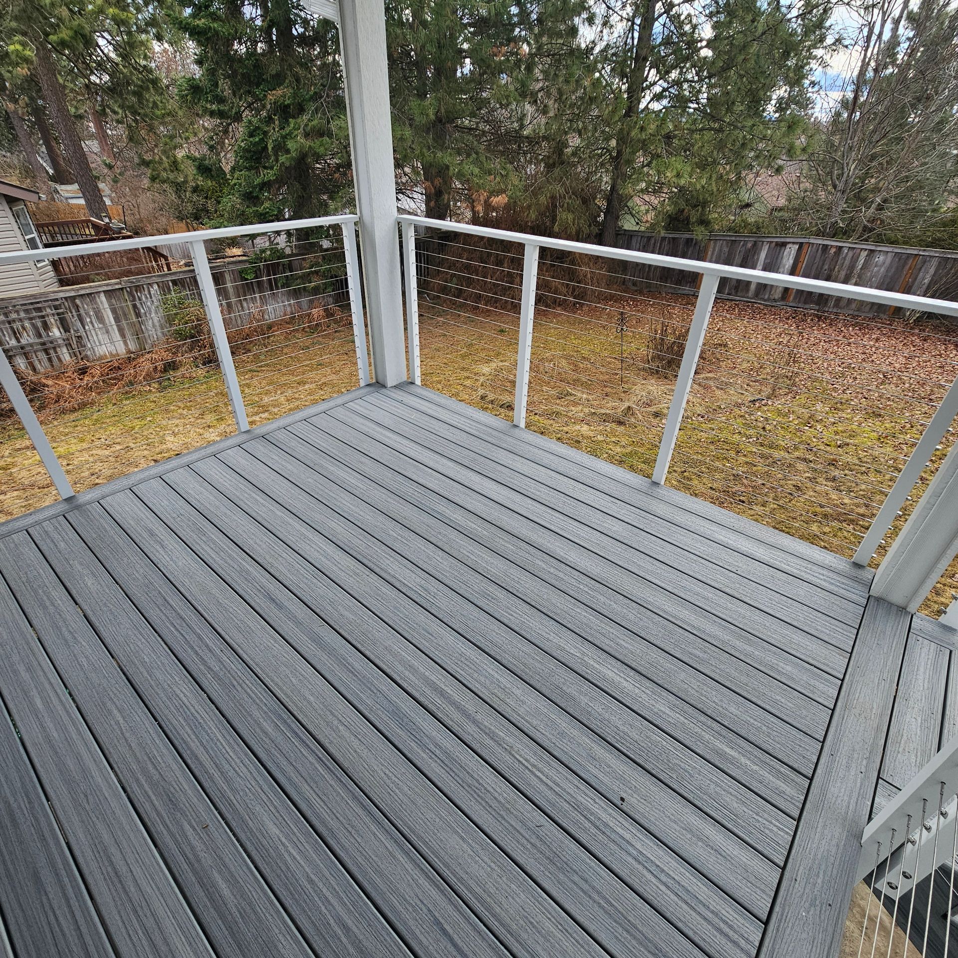 Gray composite deck with white railings, glass panels, and a yard with trees in the background.