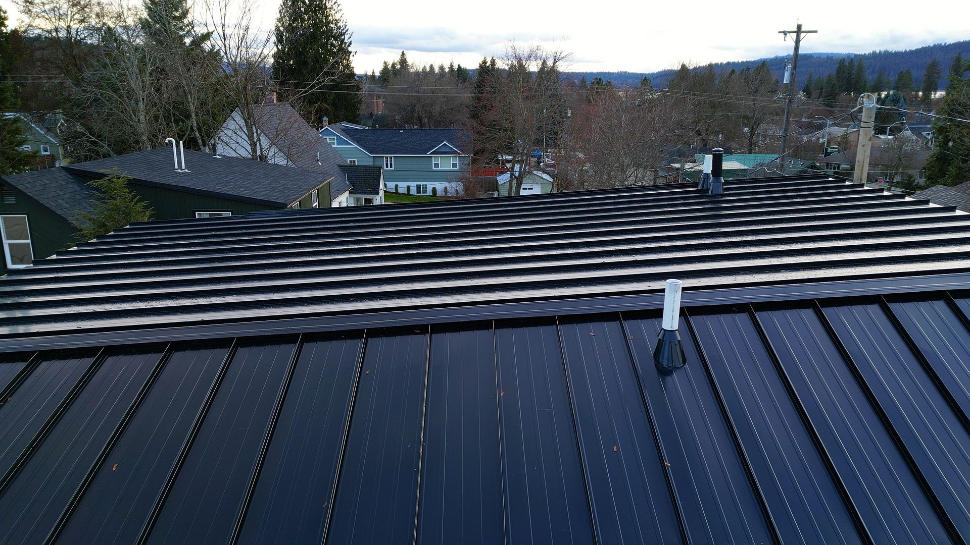 Rooftop solar panels on a residential roof, with a view of houses and trees in the background.
