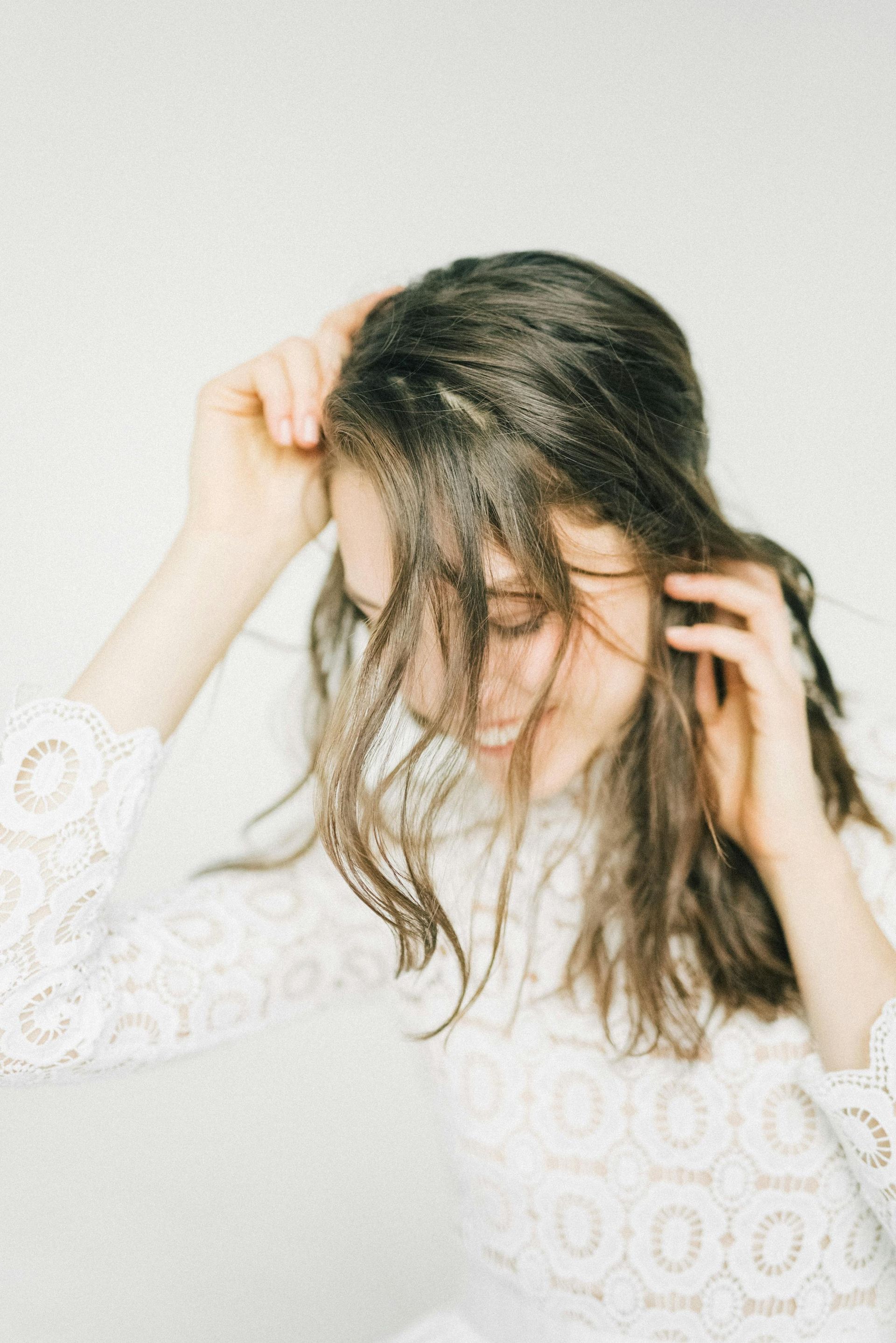 A woman in a white dress is touching her hair.