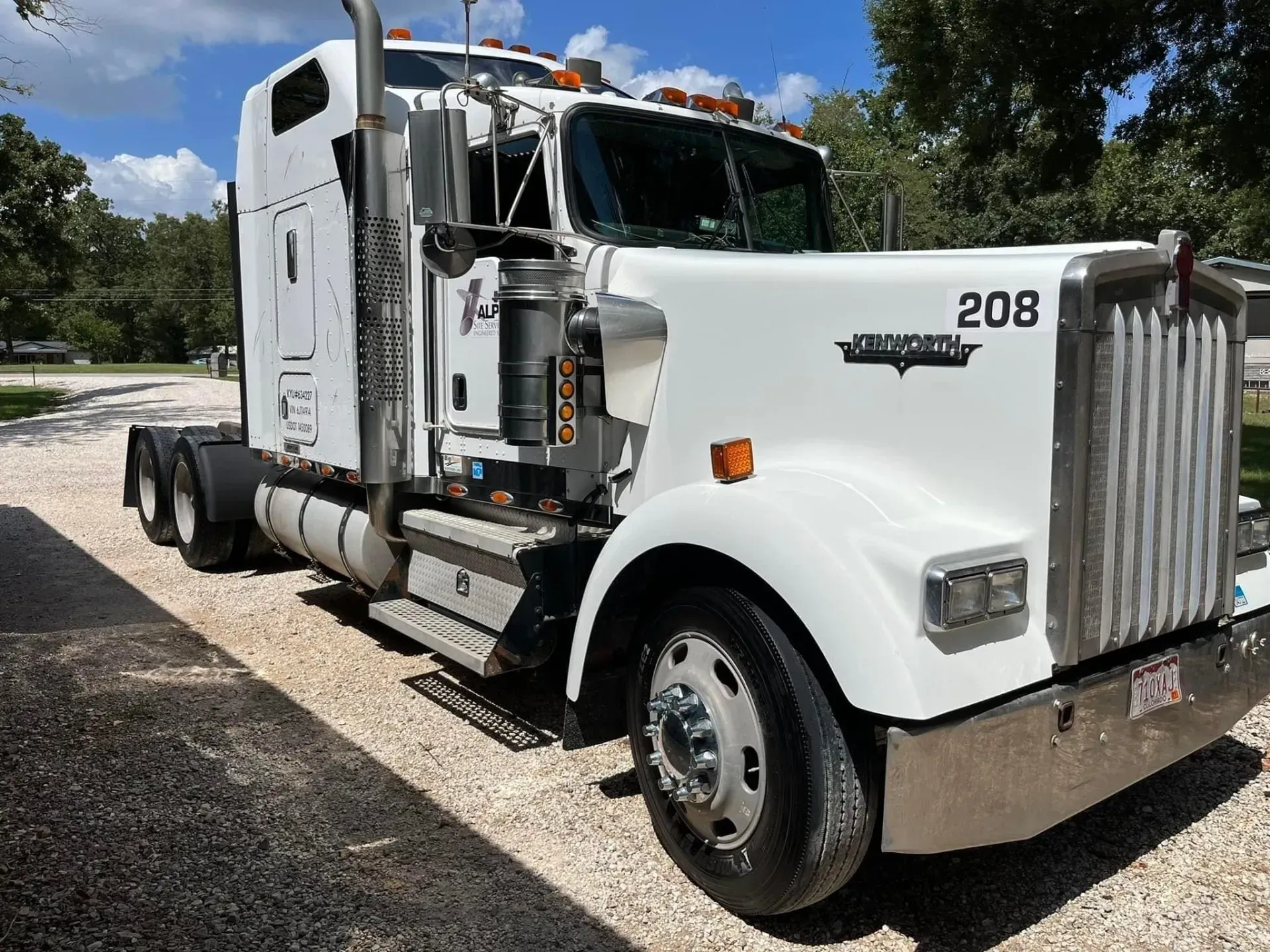 A white semi truck with the number 208 on the front is parked in a gravel driveway.