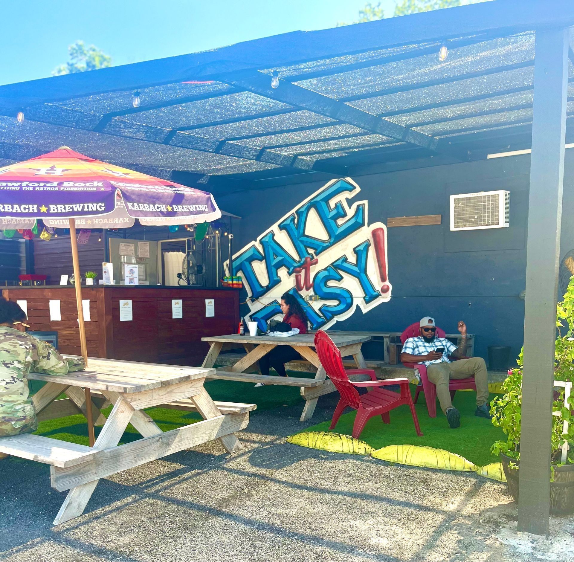 A man sits at a picnic table in front of the Take it Easy Patio Bar at Spot58 Car Wash and Detail Center in North Houston