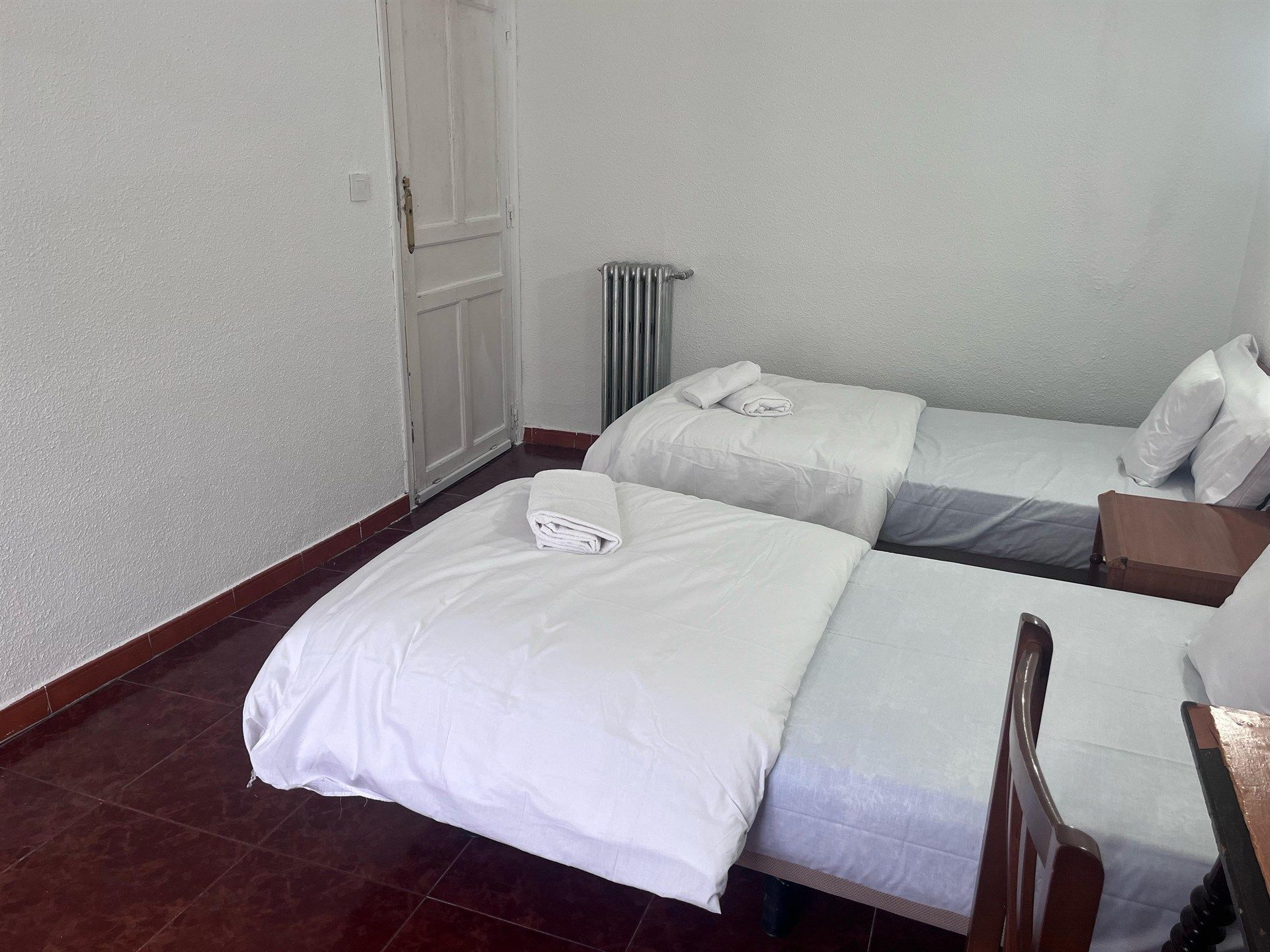 A bedroom with two beds , a desk and a radiator.
