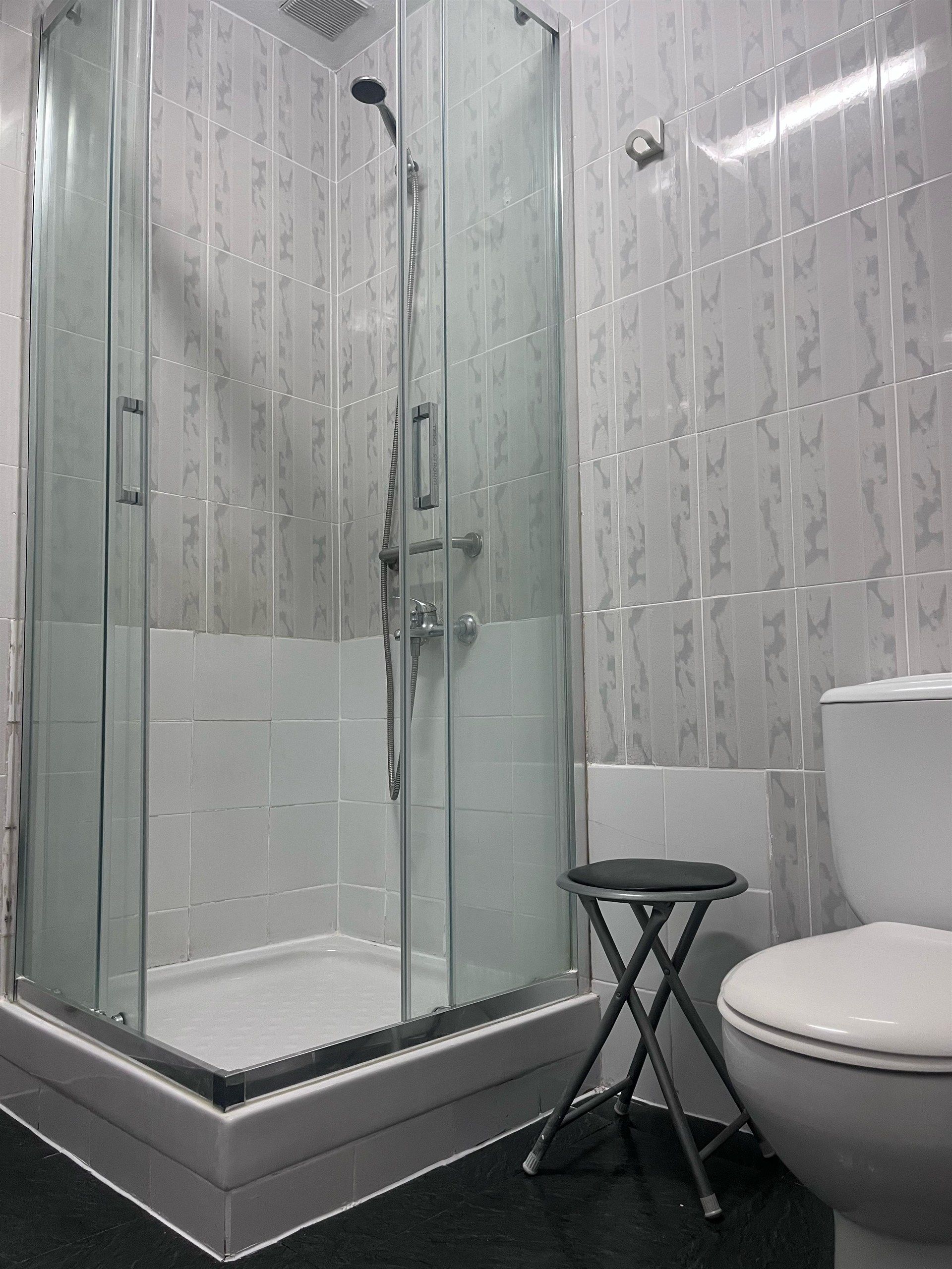 A bathroom with a toilet a shower and a stool