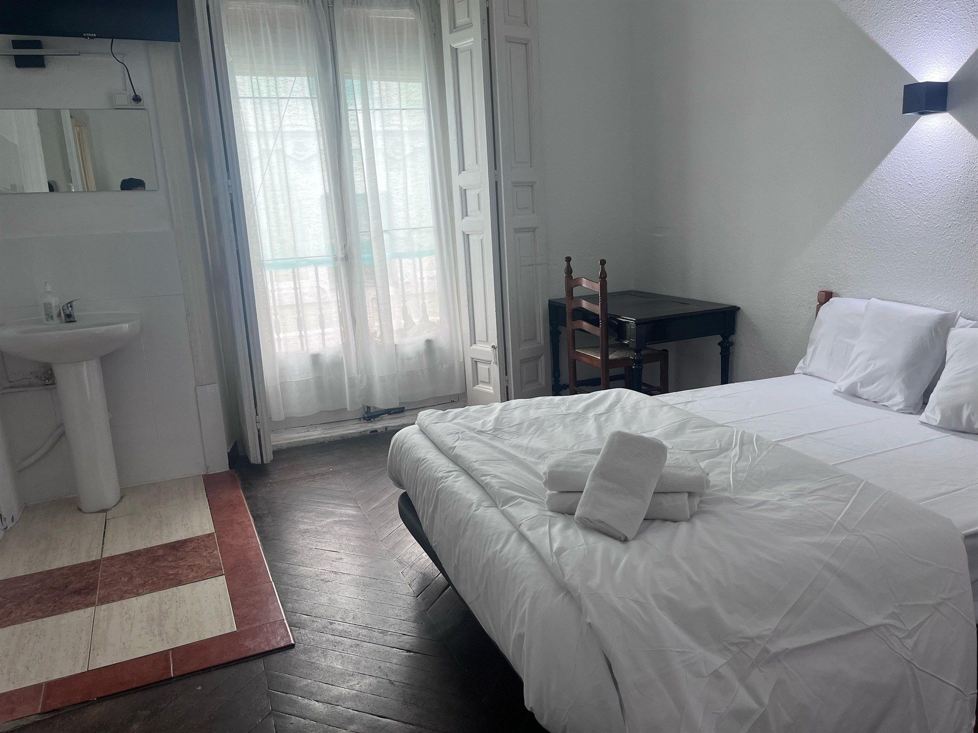 A hotel room with a bed , desk , chair and sink.