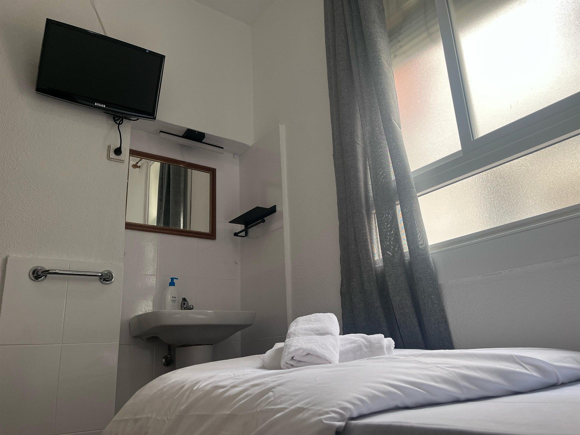 A hotel room with a bed , sink , television and window.