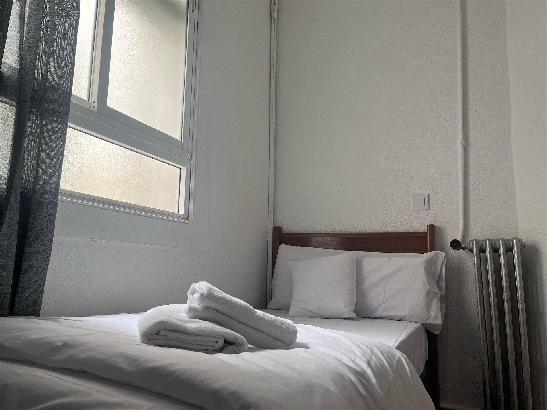 A bed with white sheets and pillows in a small bedroom next to a window.