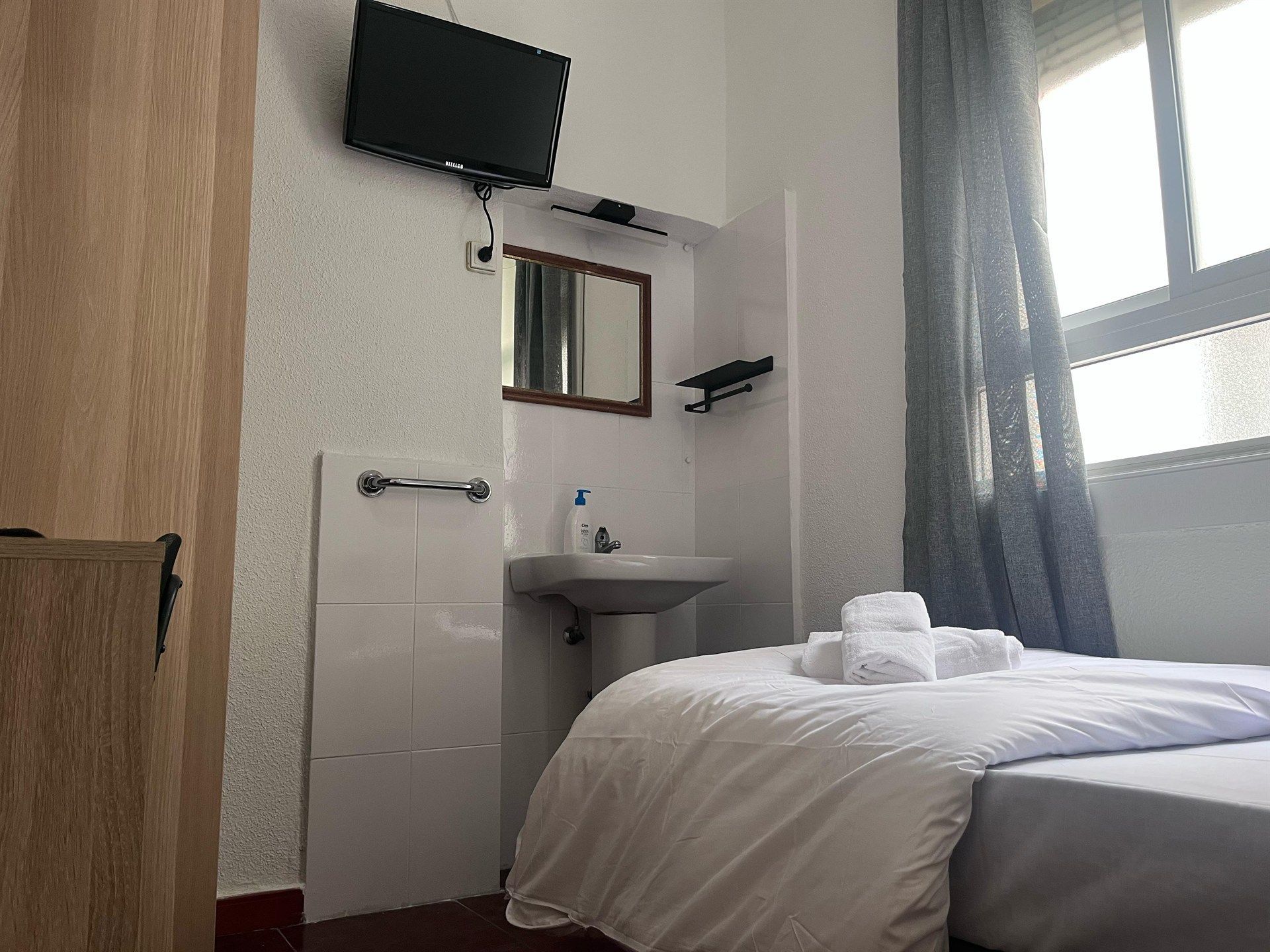 A hotel room with a bed , sink , television and mirror.