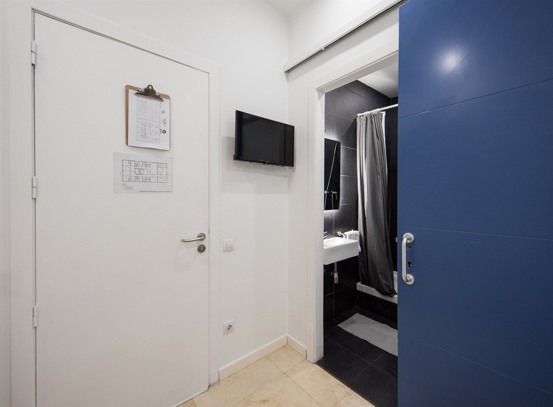 A bathroom with a blue door and a television on the wall.