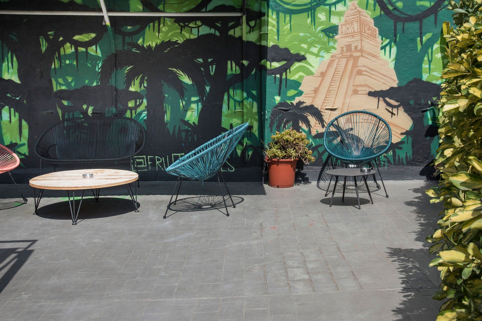 A patio with chairs , a table and a mural on the wall.