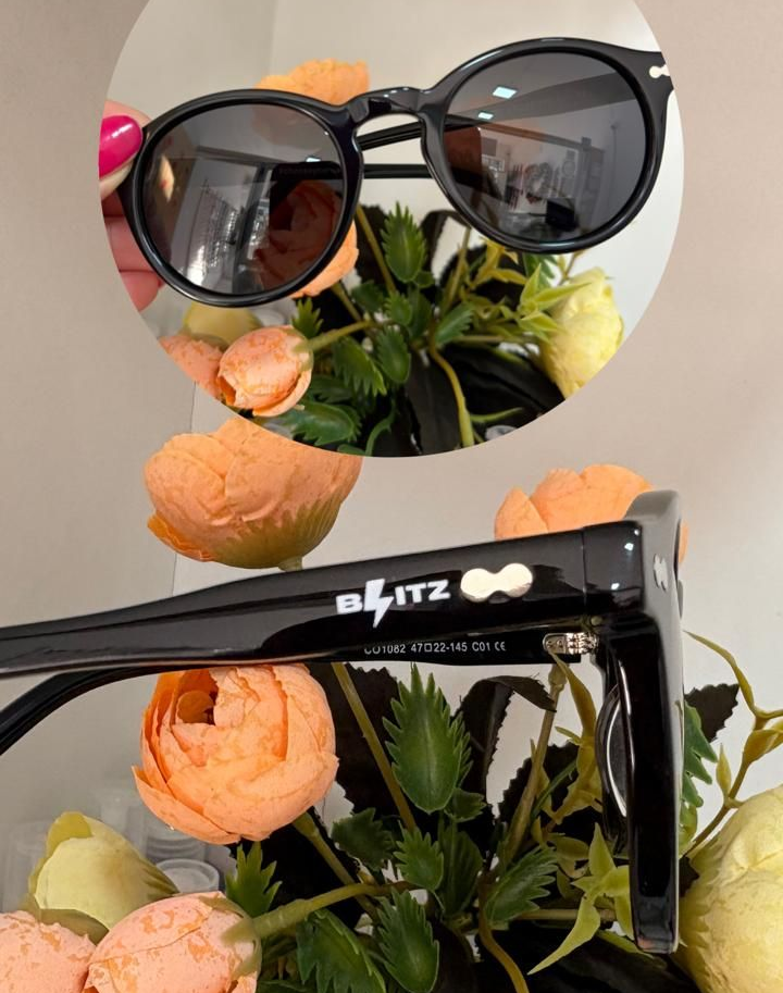 Gafas de sol negras con lentes redondas; se muestran delante de flores color melocotón.