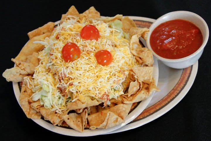 Nachos topped with shredded cheese and cherry tomatoes, served with a side of red salsa