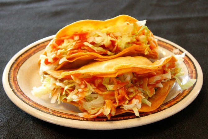 Cheesy enchiladas with red sauce and shredded lettuce on an oval plate