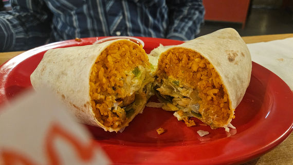 Cut burrito on a red plate, showing orange filling inside a tortilla wrap.