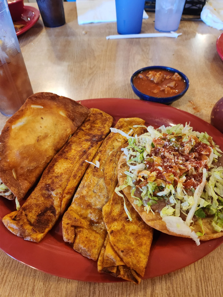 Red plate of toasted bread and a taco topped with lettuce, cheese, and salsa on a table