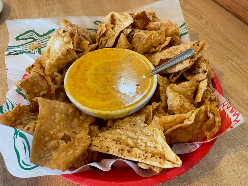 Assorted fried appetizers with a small bowl of orange dipping sauce on a paper-lined tray