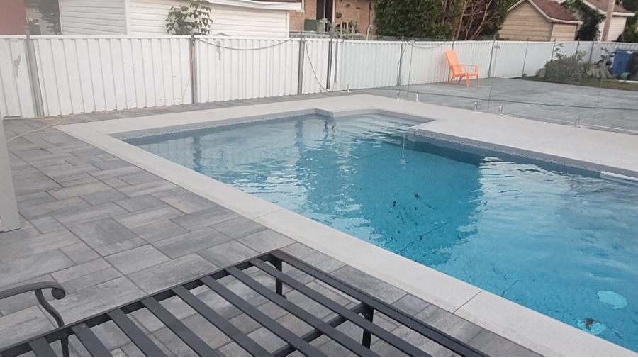 Une grande piscine est entourée d'une clôture et d'un patio.