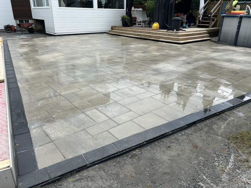 Un patio avec une bordure noire est en cours de construction devant une maison.