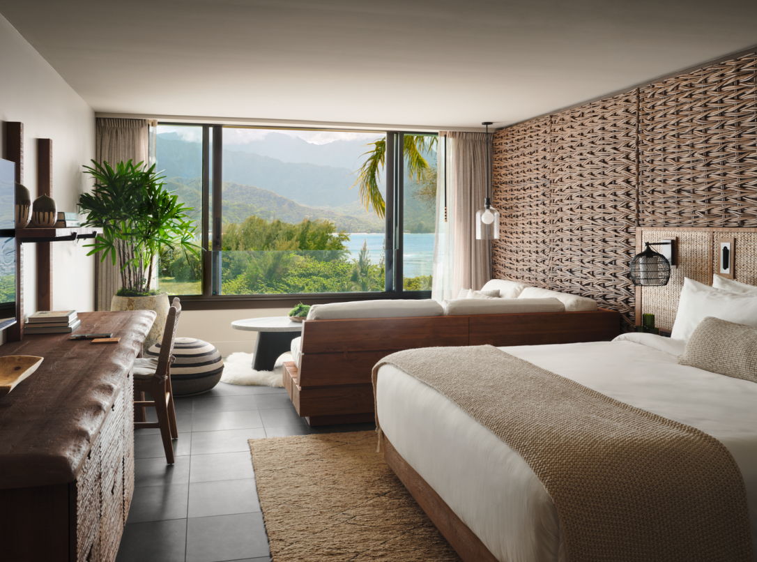 Hotel room with a bed, desk, and a sofa overlooking a scenic view of a bay.