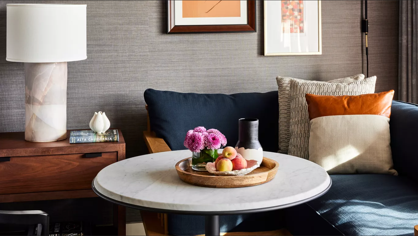 Cozy room with round table set for snacks, flowers, pillows, lamp, artwork, and dark blue couch.