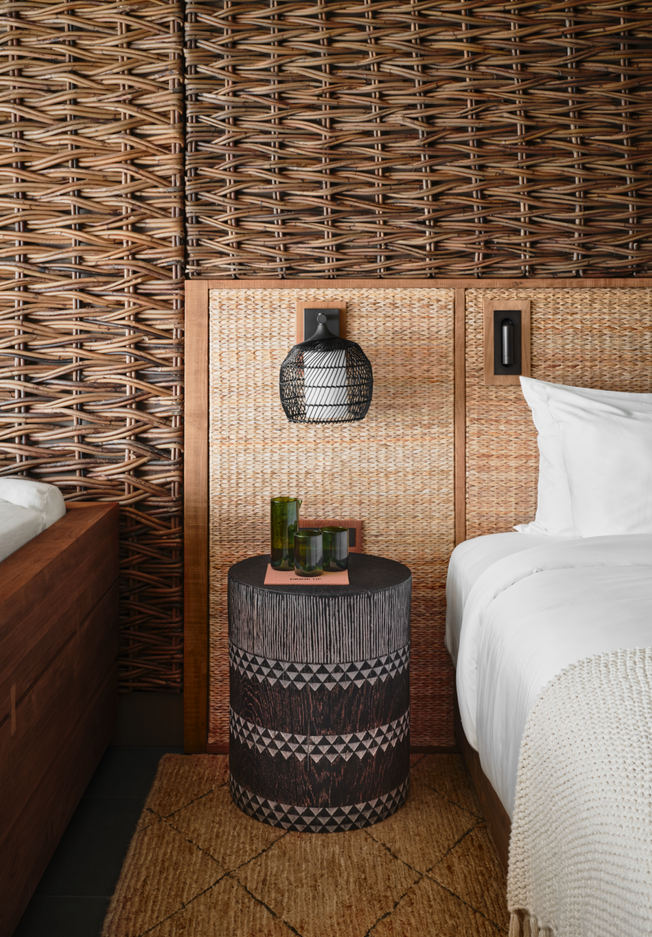 Bedroom with woven headboard and walls, side table with decor, and bed with white linens.