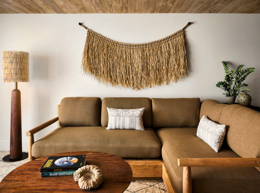 Living room with brown sectional sofa, round wooden coffee table, woven wall art, and a floor lamp.