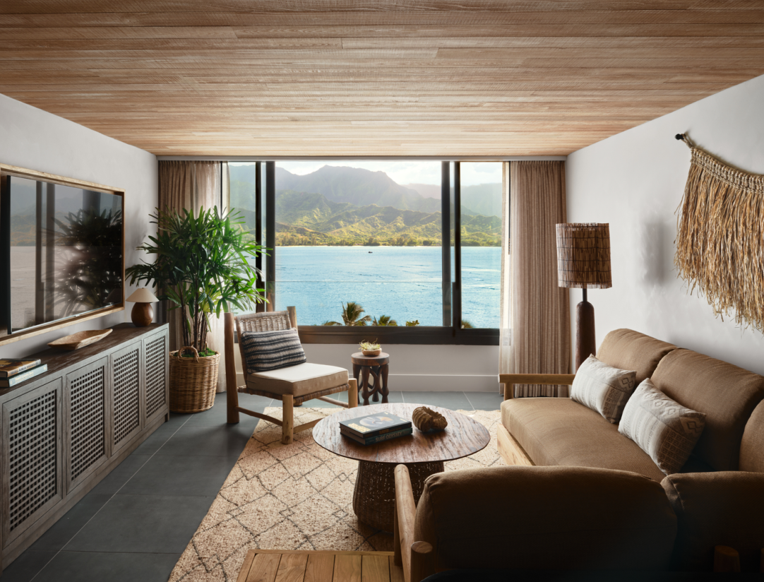 Living room with ocean view, brown sofa, wood furniture, rug, and large windows.