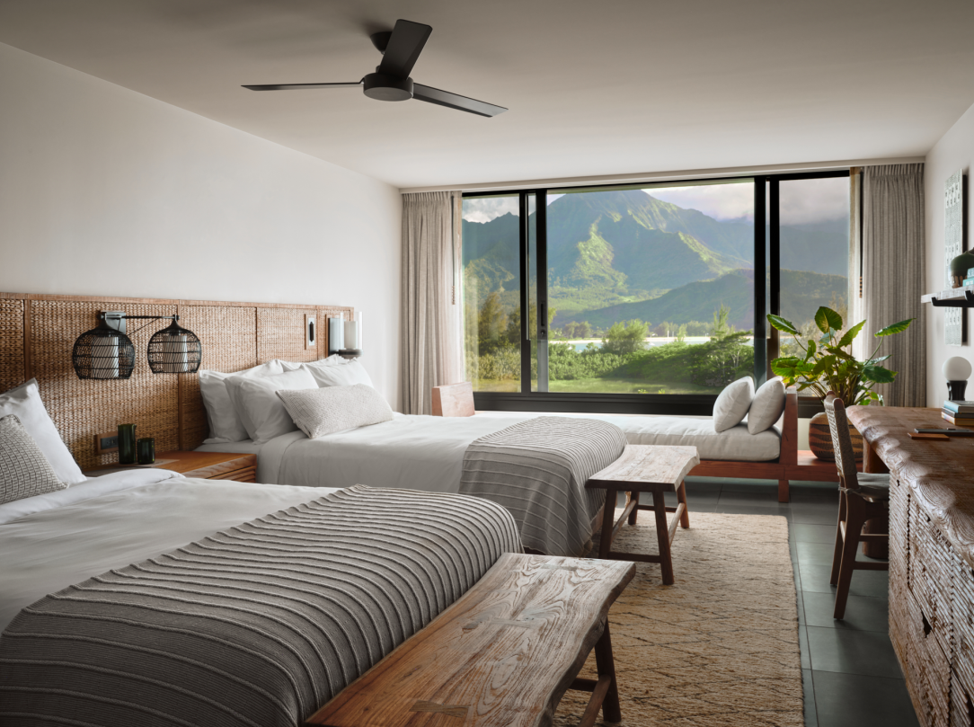 Bedroom with two beds, woven headboard, large window with mountain view, and a wooden bench.