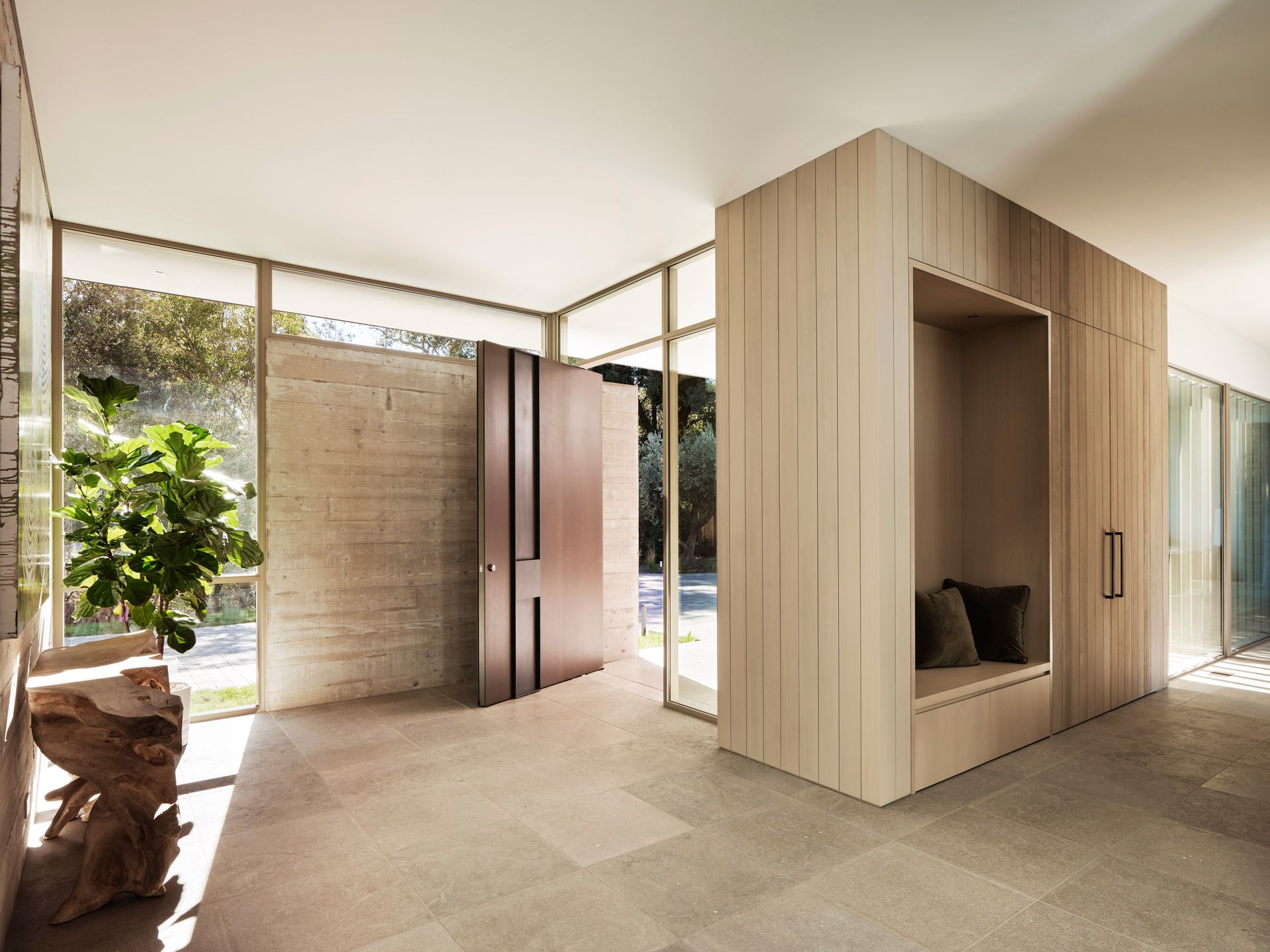 Entryway with wooden paneling, built-in bench, and large windows with greenery views.