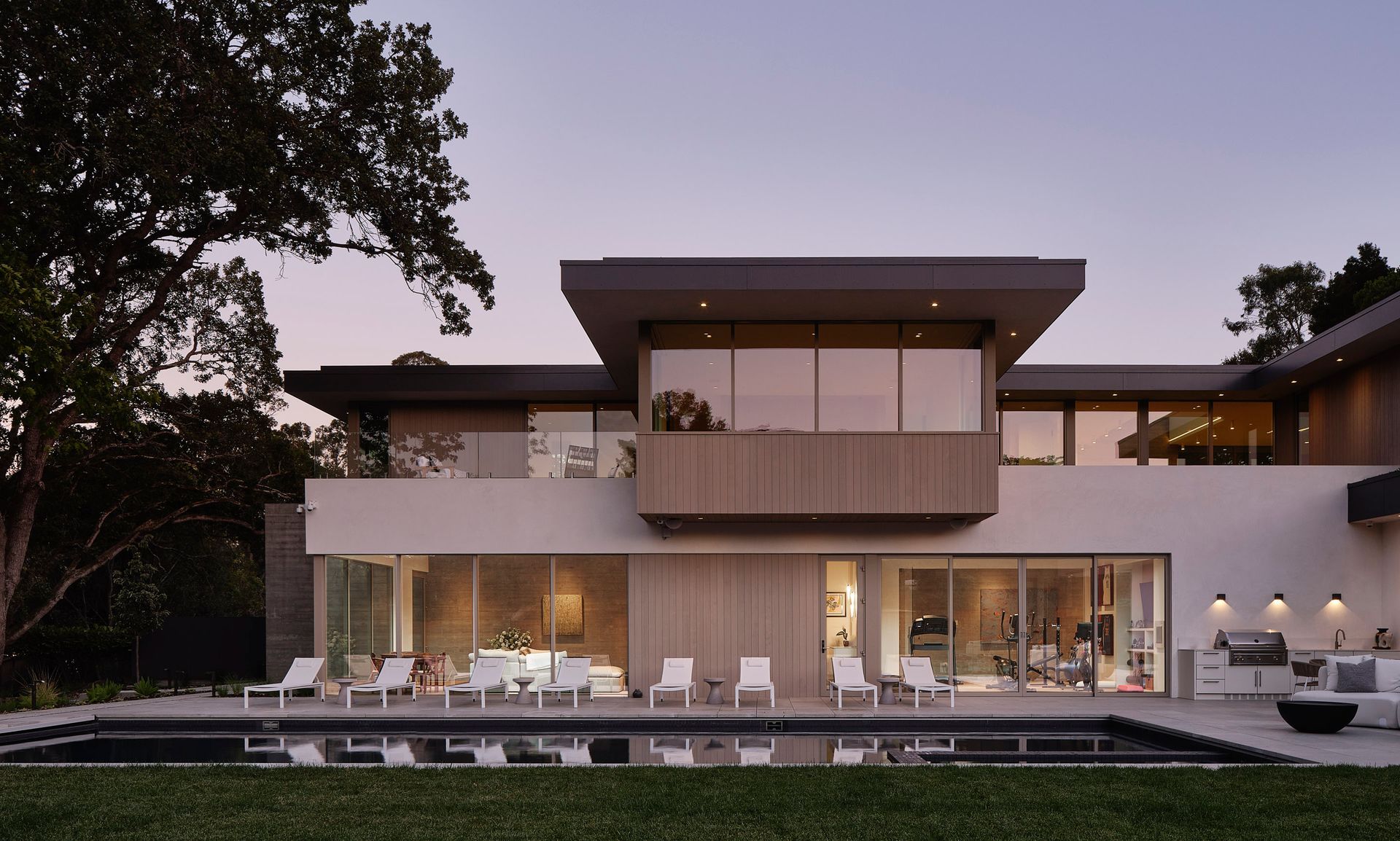 Modern house with pool, outdoor kitchen, and lounge area at dusk.