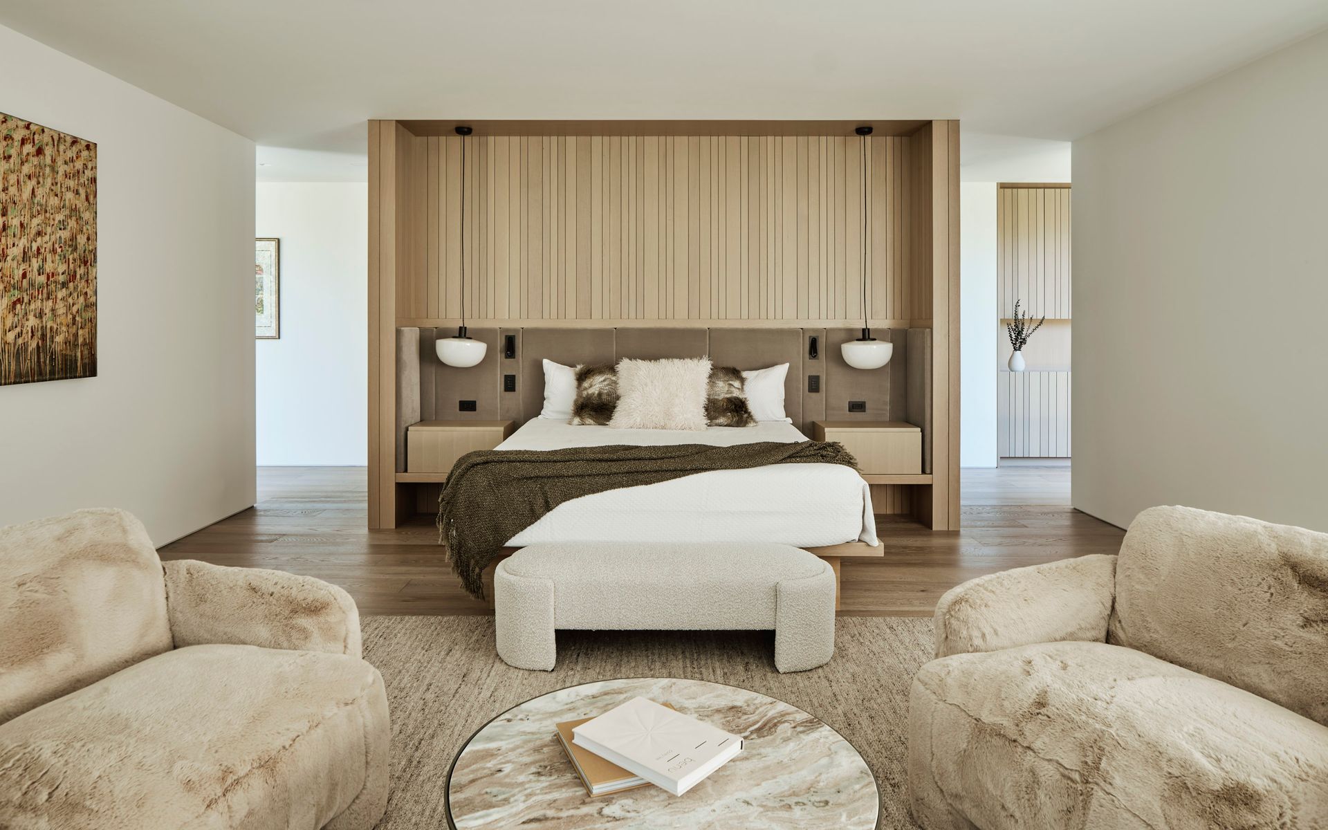 Spacious modern bedroom with bed, seating area, neutral colors, wood paneling, and a rug.