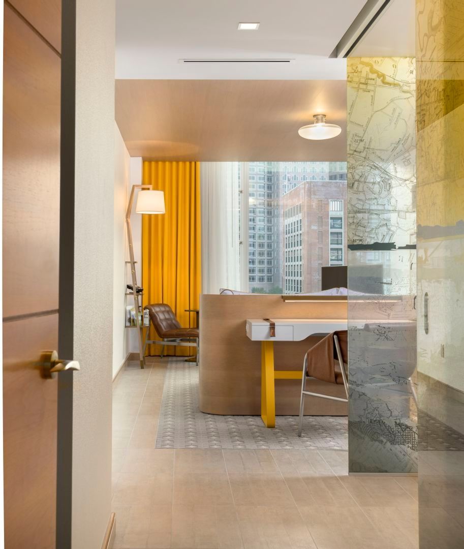 Interior view of a modern office space, featuring a desk, chair, yellow curtains, and a city view.